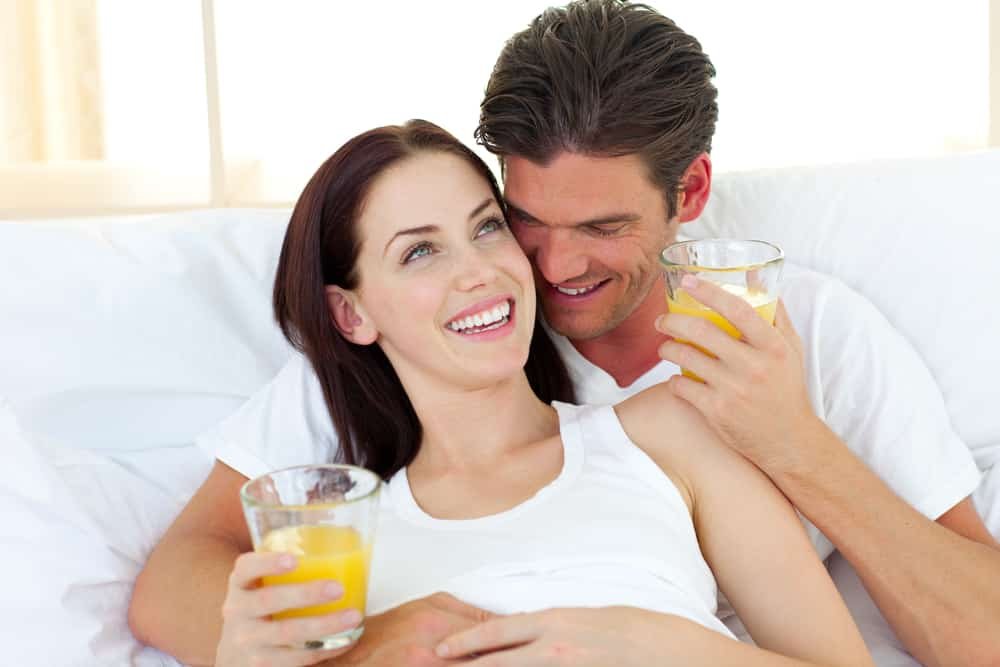 Young couple drinking orange juice lying on their bed